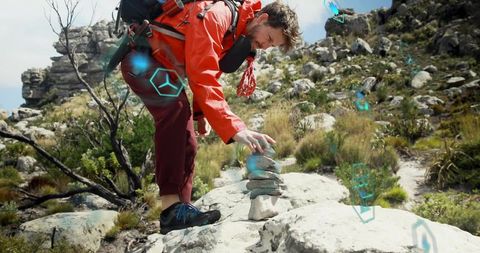 Hiker placing stone cairn on rocky ridge wearing orange jacket with blue ar holograms