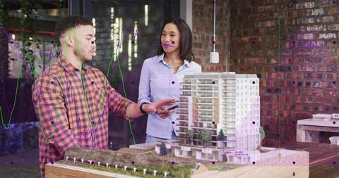 Architects collaborating over scale model with ar data visualization in industrial studio