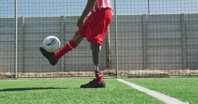 Young soccer player with prosthetic leg kicking ball on field, showing determination and athleticism. Suitable for sports, inspiration, disability awareness, and triumph over challenges themes.