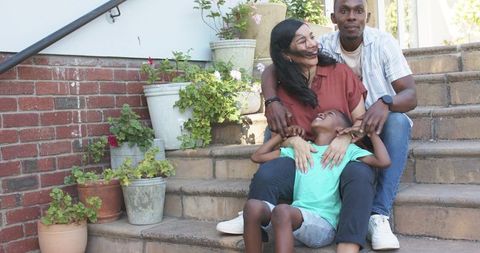 Joyful family sharing warm laughter on sunlit front steps with colorful potted plants