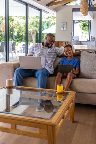 African american father and son bonding on sofa using laptop and tablet in living room