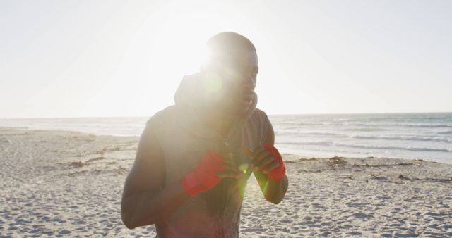 Boxer engaging in training routine on sandy beach with sunlight casting a bright glow. Ideal for fitness-themed websites, exercise guides, motivational posters, or articles on outdoor activities and health benefits of beach workouts.