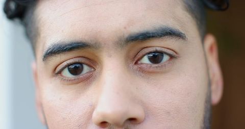Close-up male headshot showing skin texture, brown eyes, subtle stubble, soft light