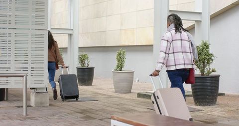 Senior African American Woman Walking with Female Friend Pulling Suitcases on Urban Walkway