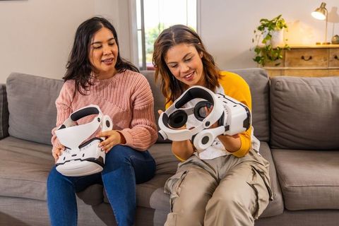 Diverse friends testing white vr headsets on couch in modern living room daylight