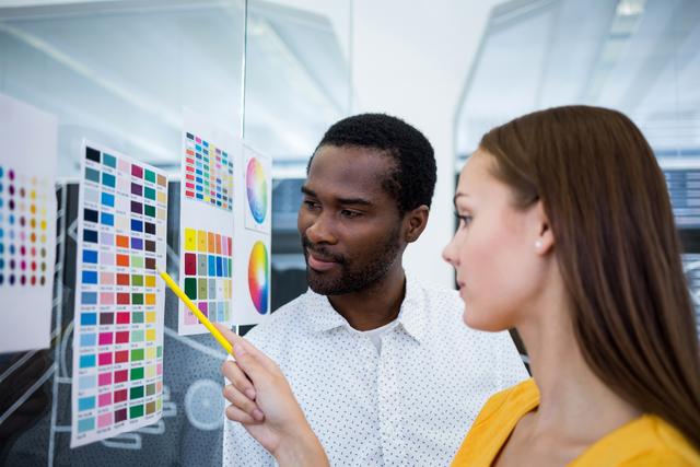 Male and female graphic designers interacting over color chart in office