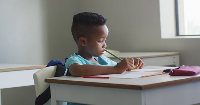 Young African American student is focused on studying at desk in classroom. Ideal for educational materials, school promotions, and websites dedicated to learning and child development.