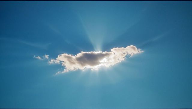 Radiant Sunbeams Streaming Behind Fluffy Cloud in Clear Sky