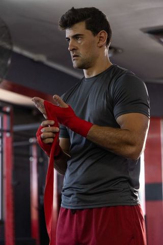 Focused male boxer wrapping red hand wraps preparing for intense training session