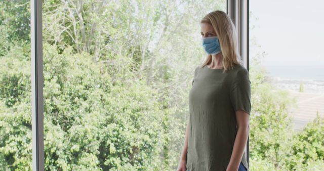 Woman Wearing Face Mask Standing by Window, Green Outdoor View - Download Free Stock Images Pikwizard.com