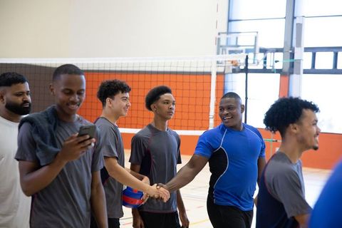 Diverse male teens shaking hands showing sportsmanship after indoor volleyball game