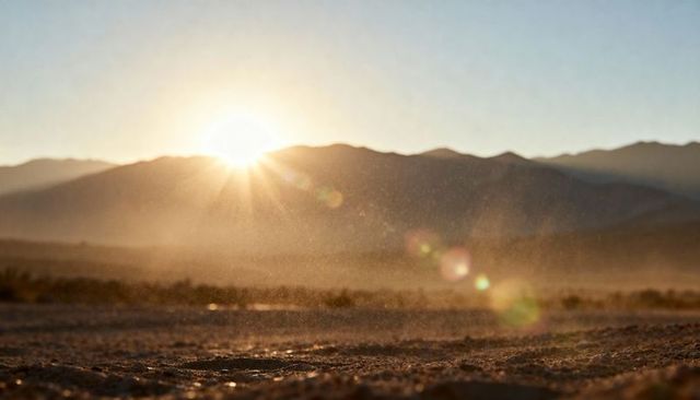 Golden desert sunrise over mountain ridge with dust haze, sunburst lens flare, textured sand