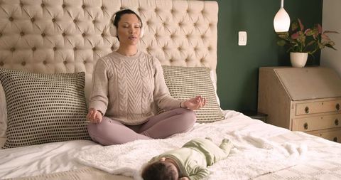 Asian Mother Meditating with Infant Nearby in Cozy Bedroom