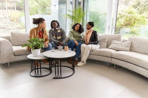 African american friends chatting on curved gray sectional sofa in bright modern lounge