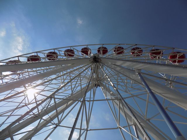 Majestic Ferris wheel towering against a clear blue sky with eight red cabins highlighted by sunlight, creating a sense of adventure and enjoyment. Perfect for use in travel blogs, amusement park promotions, family outing brochures, and summer event advertisements.