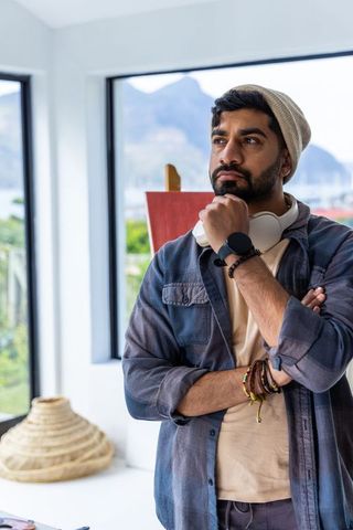 Asian artist in 30s contemplating creative project in bright waterfront studio