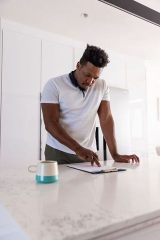 Man leaning over marble kitchen island reviewing clipboard in modern bright kitchen