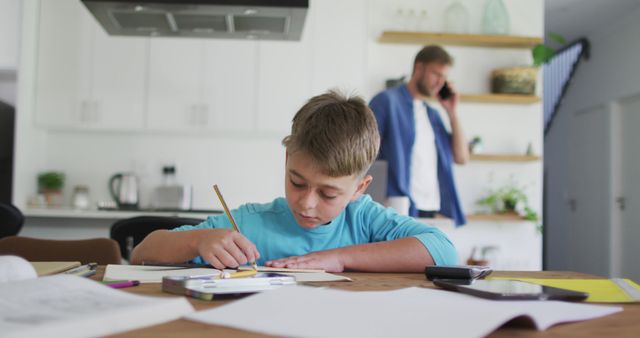 Focused caucasian boy doing homework in dinning room with father in kitchen - Download Free Stock Photos Pikwizard.com