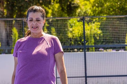 Mature woman standing on outdoor court in purple athletic shirt enjoying sunny exercise