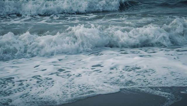 Crashing teal ocean waves rolling onto wet sandy shoreline spreading white foam moody overcast