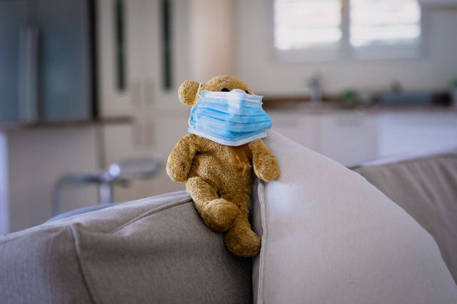 Teddy bear wearing face mask sitting on sofa. healthcare and medicine during coronavirus covid 19 pandemic.