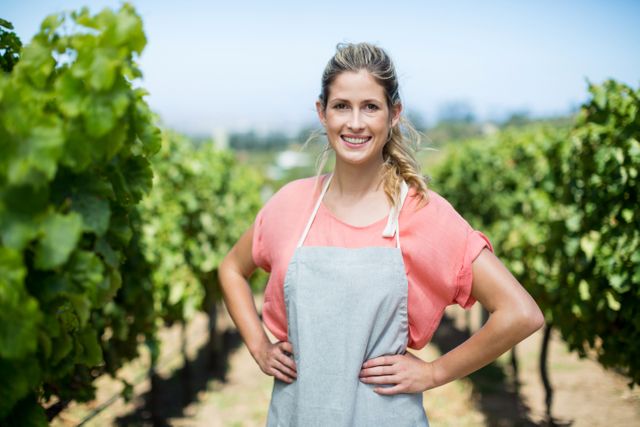 Portrait of smiling female farmer with hands on hip standing at vineyard