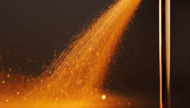 Golden glitter stream cascading diagonally with warm bokeh glow around copper rod