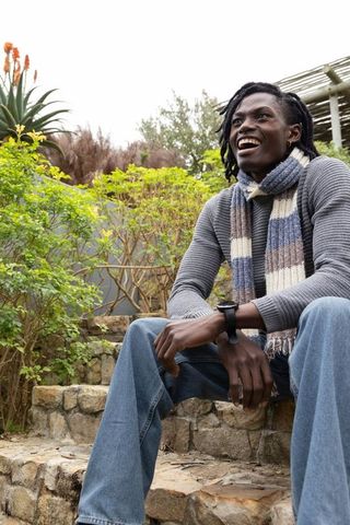 Smiling african american man sitting on stone steps in backyard wearing knit scarf