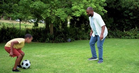 African american father teaching teen soccer skills on backyard lawn during playtime