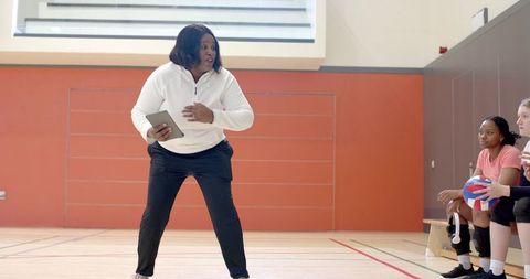 African american coach coaching teen volleyball players holding tablet on indoor gym court