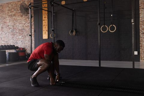 African american man crouching and preparing battle ropes in industrial gym wearing red shirt