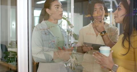 Diverse team collaborating at glass wall with diagrams, tablet and coffee for planning