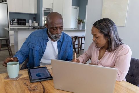 Senior couple reviewing retirement finances at kitchen table with laptop and tablet