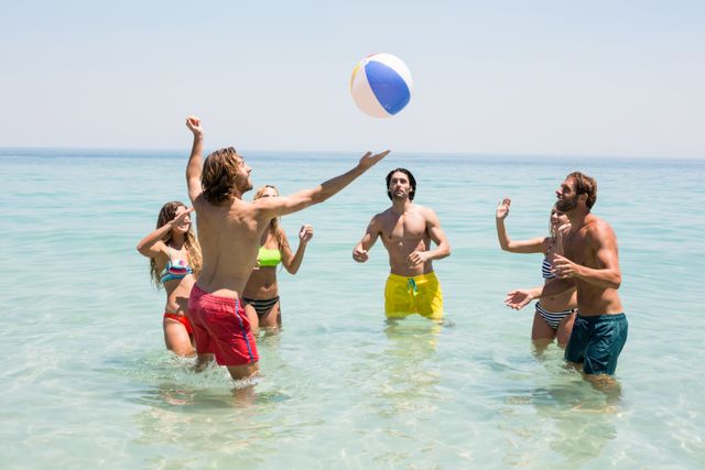 Group of friends enjoying a sunny day at the beach, playing with a beach ball in the sea. Perfect for promoting summer vacations, beach activities, travel destinations, and outdoor fun. Ideal for use in advertisements, travel brochures, social media posts, and lifestyle blogs.