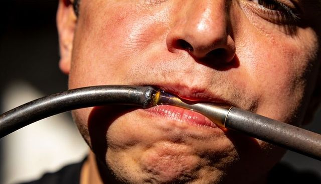Closeup workshop worker pressing metal tubes between lips showing soldered brazed joint