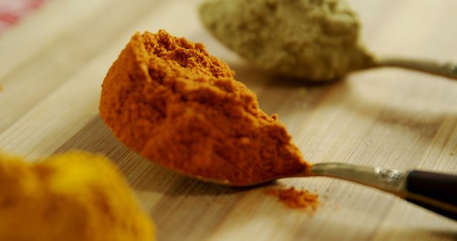 Image capturing close-up view of various spices including red chili powder and turmeric in spoons on wooden surface. Ideal for use in cooking blogs, recipe websites, culinary magazines, and food-related advertisements.