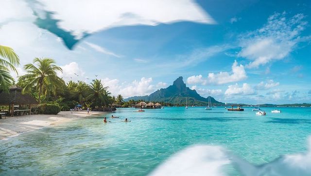 Turquoise lagoon with jagged volcanic peak, overwater bungalows and palm-fringed beach resort