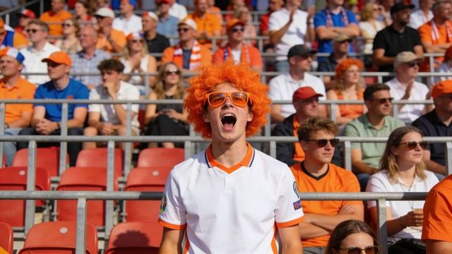 Gameday cheer: orange-wigged fan cheering loudly in stadium crowd wearing white jersey