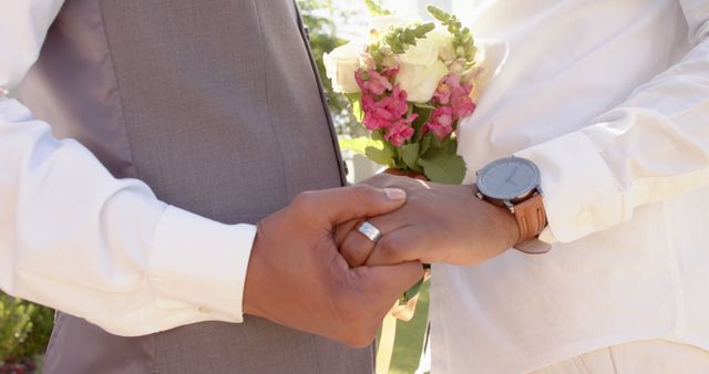 Happy diverse gay male couple holding hands outdoors in the sun. Togetherness, relationship, love and domestic life, unaltered.