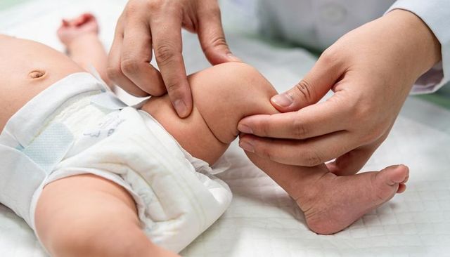 Pediatrician examining newborn knee during routine infant wellness check