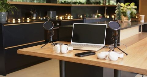 Recording podcast on communal wooden table with laptop, microphones, headphones
