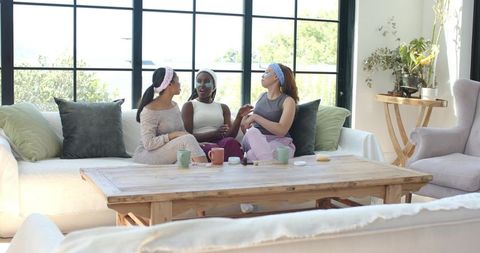 African american women relaxing on sofa applying face masks and eye patches