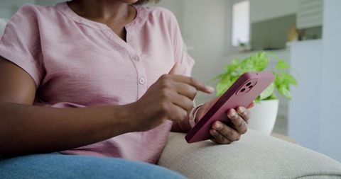 Woman tapping smartphone on couch in cozy open-plan living space using mauve case