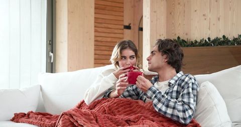 Couple Enjoys Cozy Drinks under Blanket on Sofa