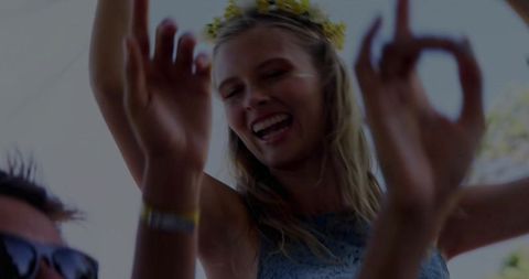 Sunlit festival joy dancing blonde woman wearing flower crown amid blurred hands