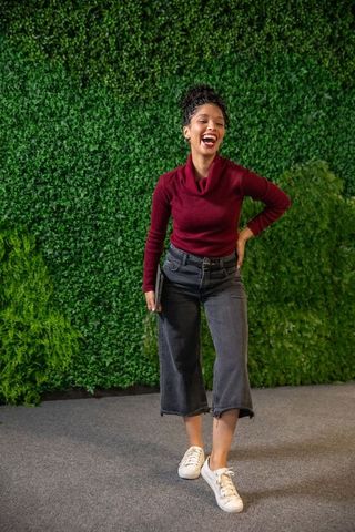 African american woman laughing and holding laptop wearing burgundy sweater by green wall