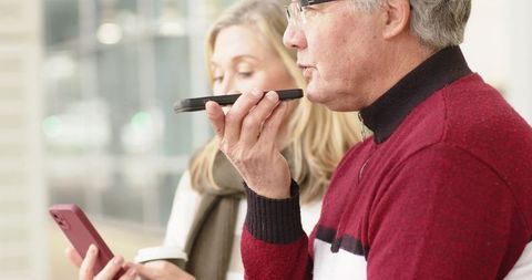Mature couple using voice assistant and smartphone in bright modern glass atrium