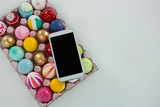 Mobile kept on painted Easter eggs in egg carton on white background