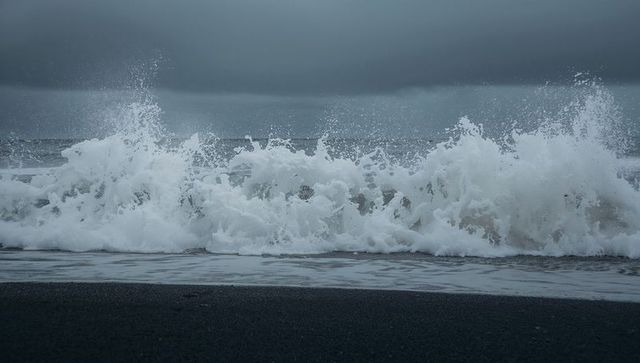 Stormy waves crashing on black sand beach, foamy surf splashing, overcast coastal mood