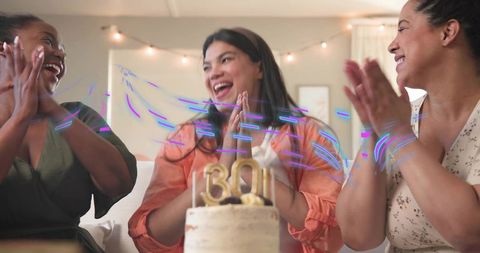 Friends celebrating 30th birthday at home clapping around cake with gold 30 topper